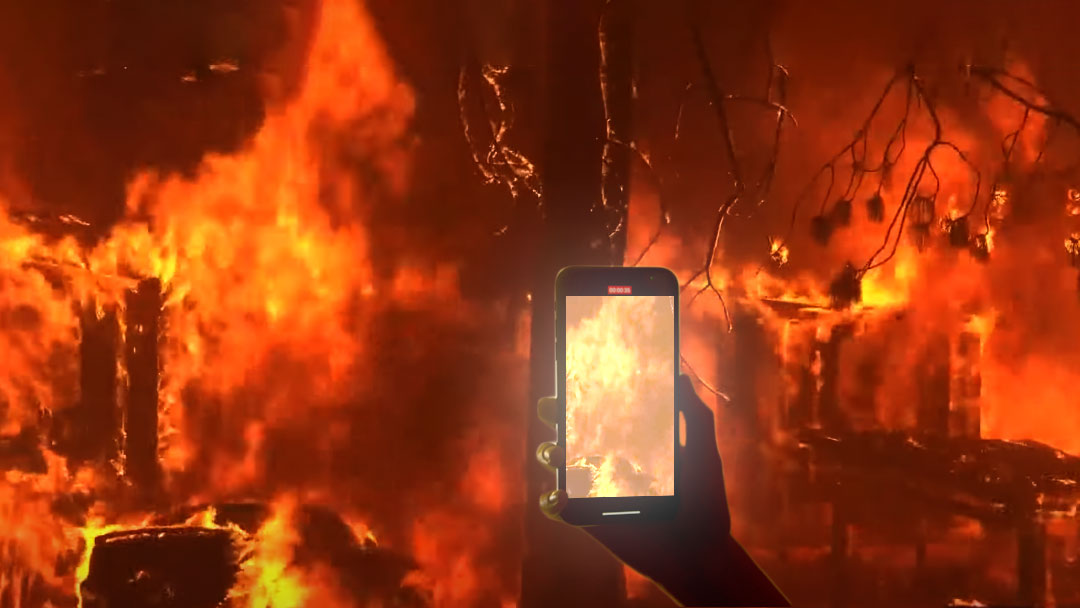 Photo of a fire and a person holding a smartphone filming it